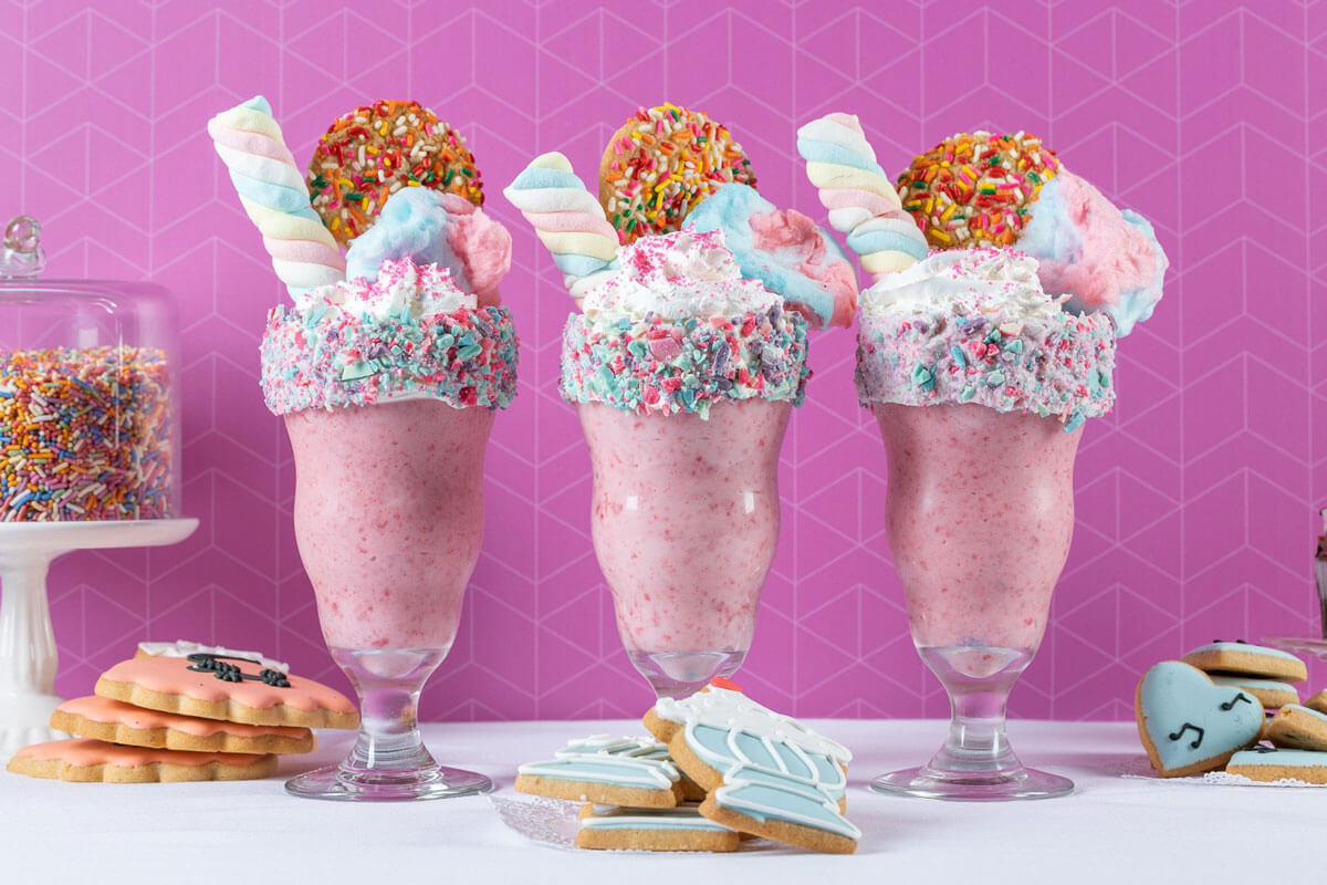 Three pink milkshakes with sprinkles and cookies