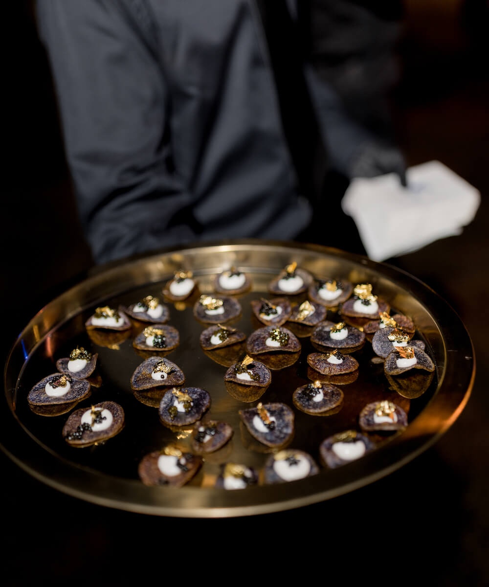gold platter of small bites being held by a server dressed in black