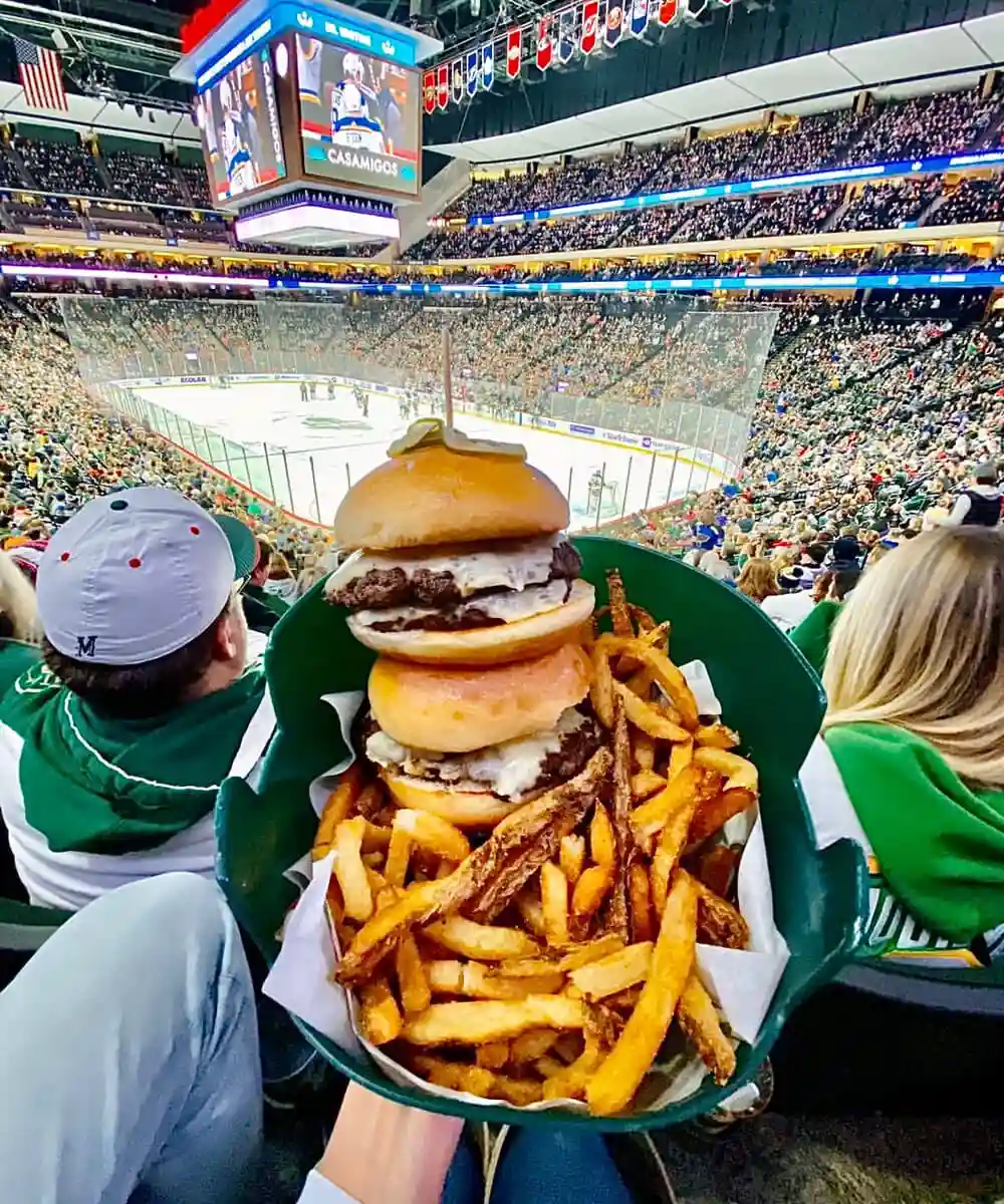 A diner holding a burger and fries platter in the foreground of a stadium crowd