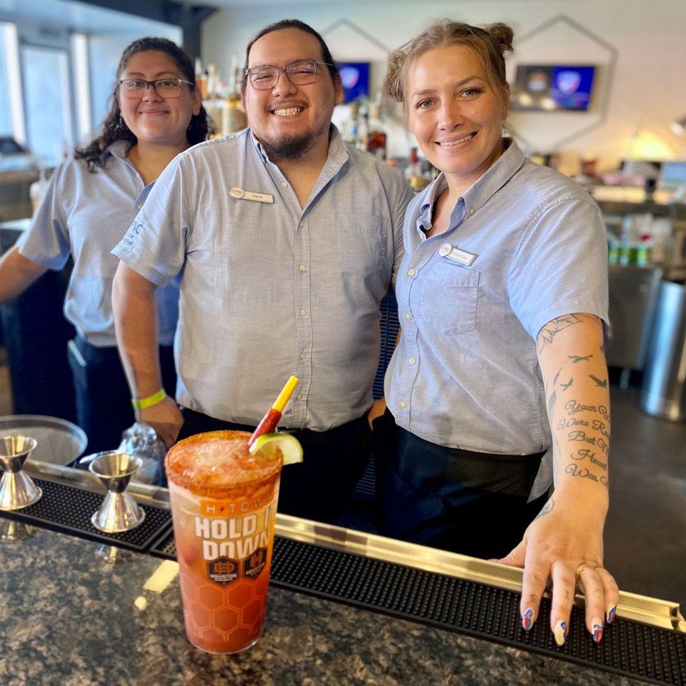 Three smiling servers behind a bar