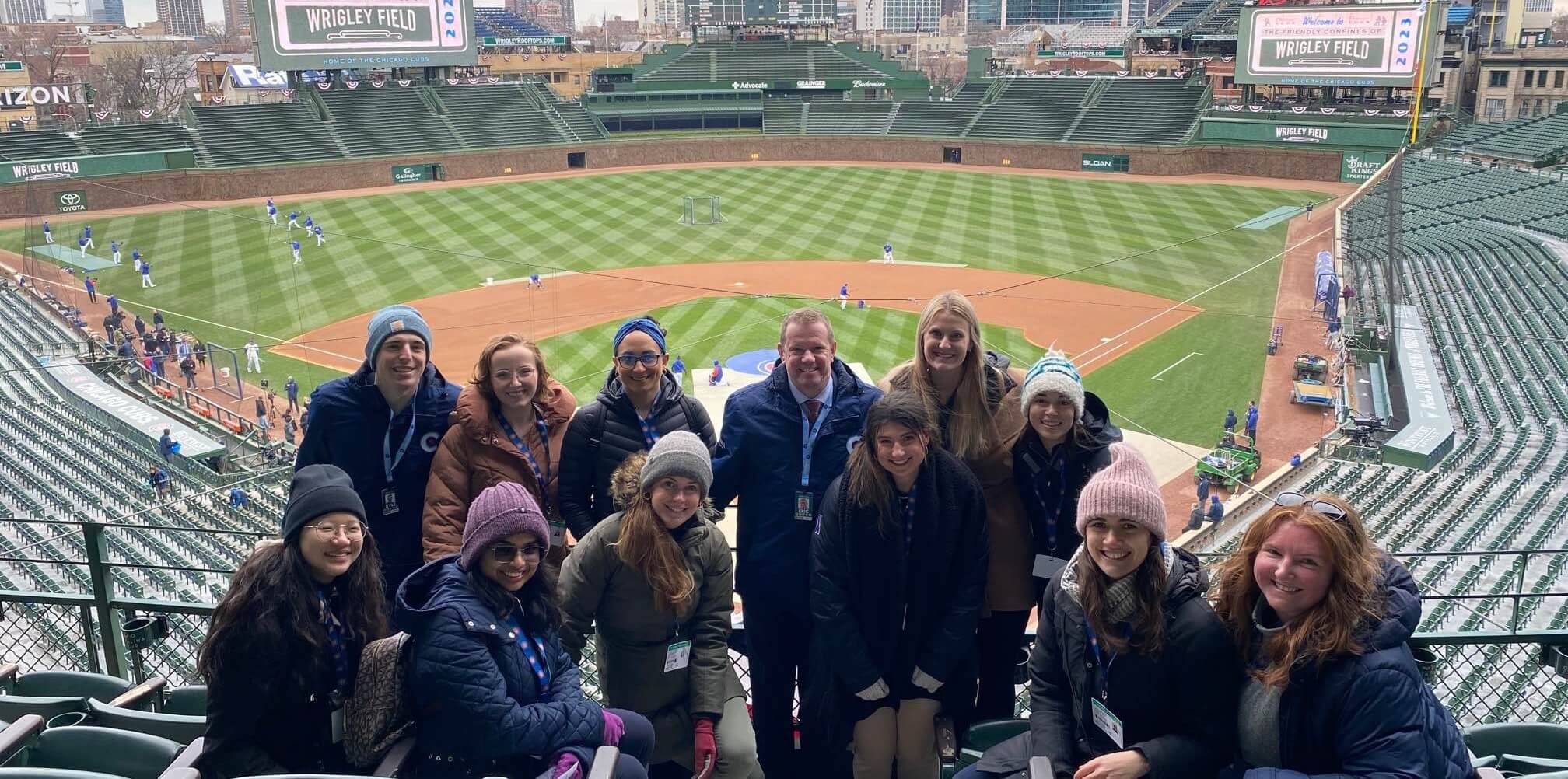 A group of employees posing in front of a large baseball stadium - Desktop Version